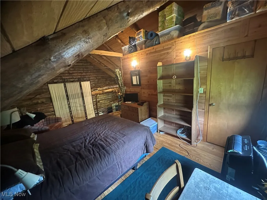 Bedroom with hardwood floors, log walls, and wooden walls
