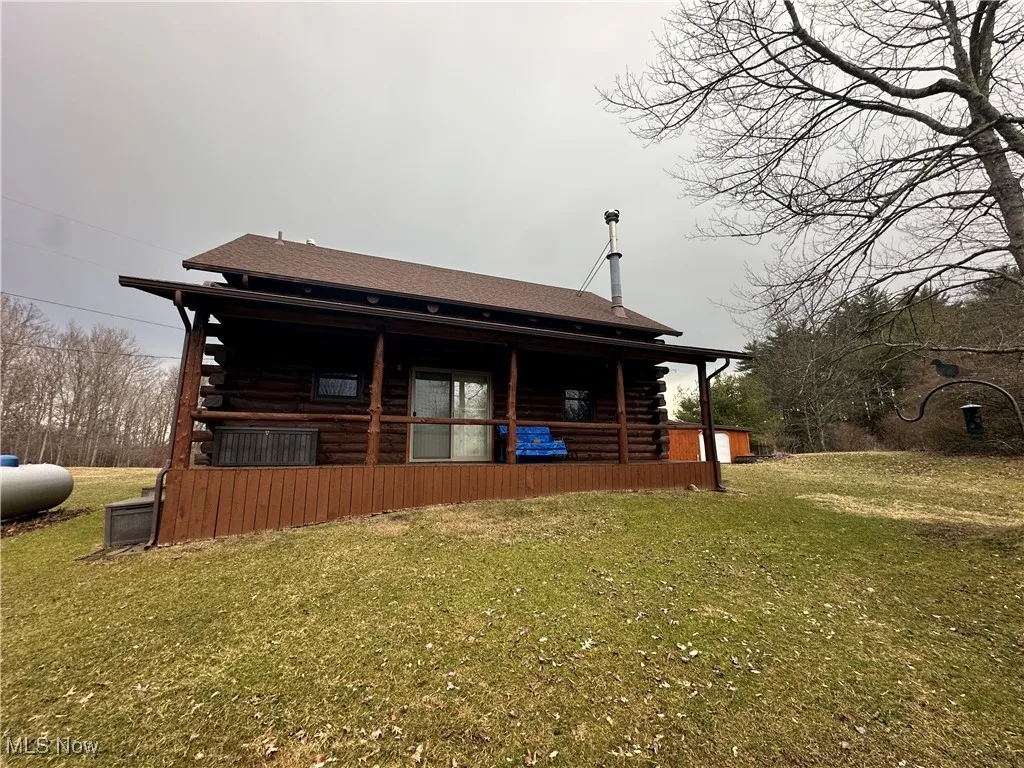 Rear view of property with log siding, covered porch, and a lawn
