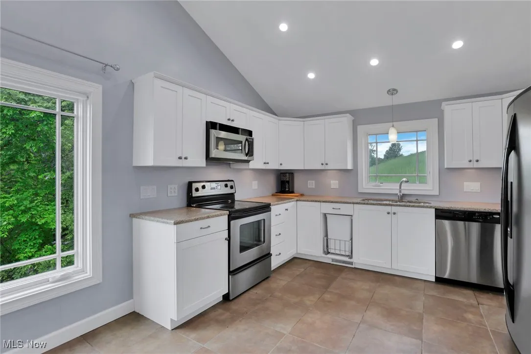 Kitchen with stainless steel appliances, a sink, plenty of natural light, white cabinetry, and lofted ceiling