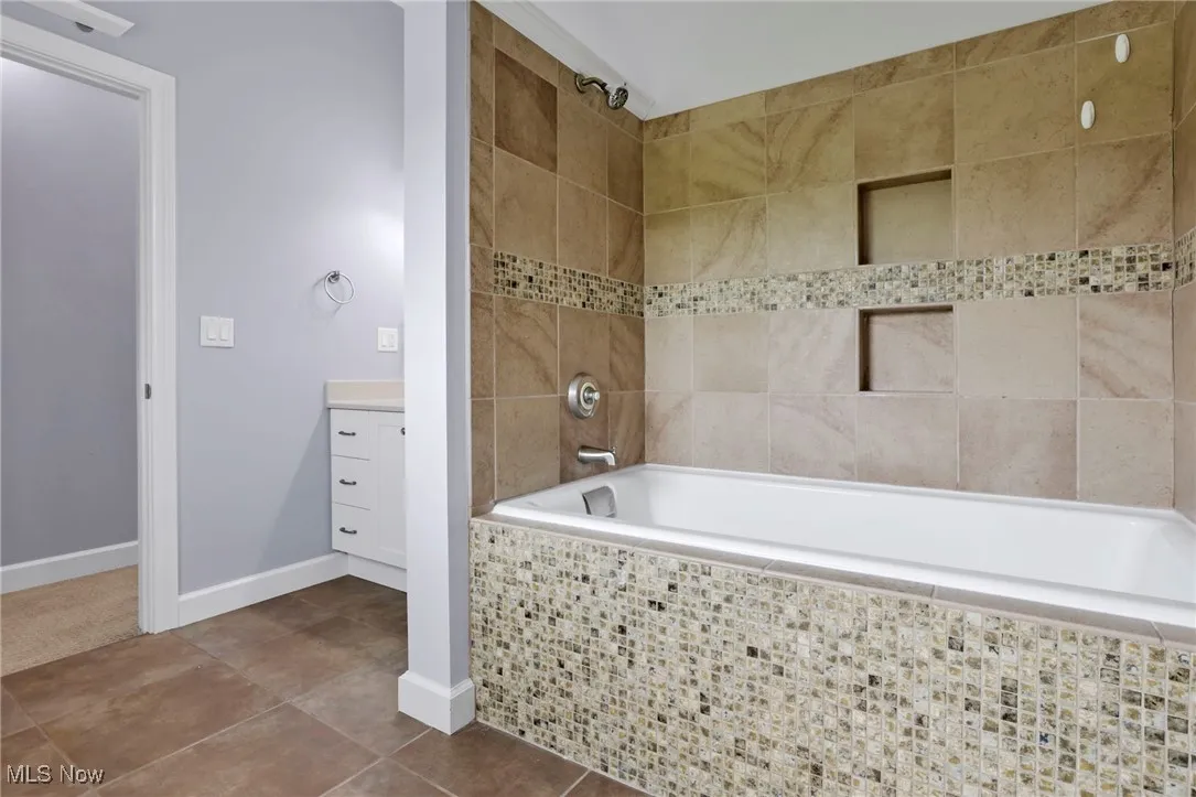 Bathroom featuring tiled shower / bath combo, vanity, baseboards, and tile patterned floors