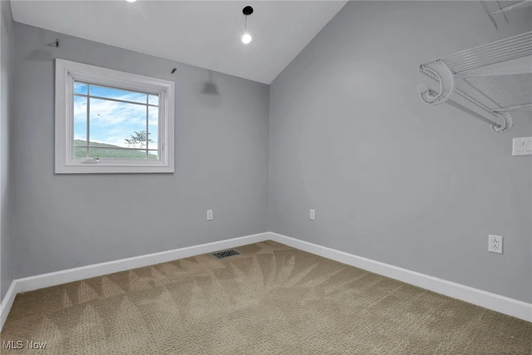 Spare room featuring carpet floors, baseboards, and lofted ceiling