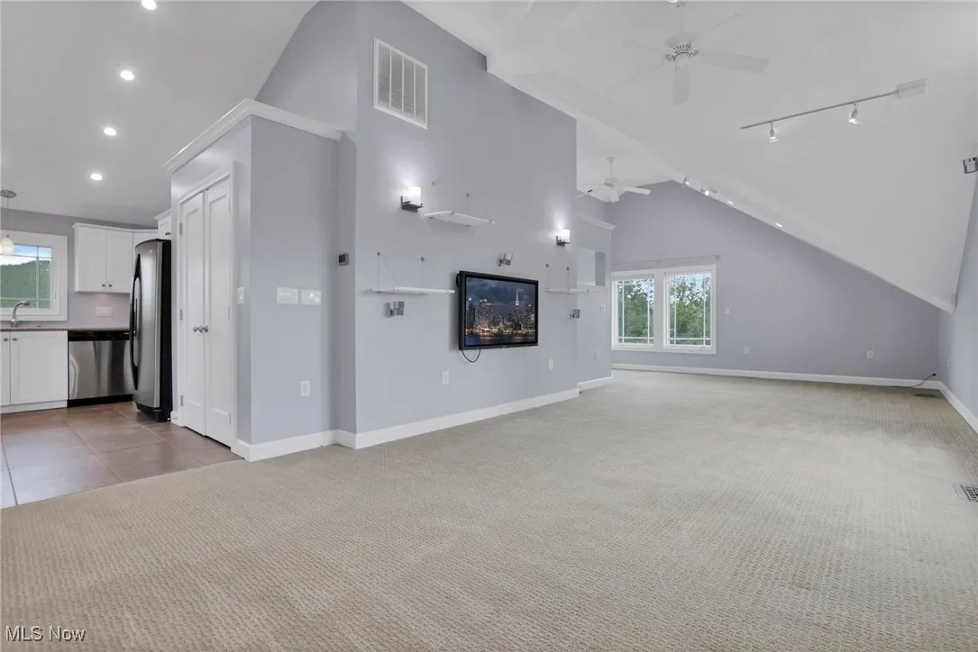 Unfurnished living room featuring ceiling fan, light carpet, baseboards, recessed lighting, and lofted ceiling