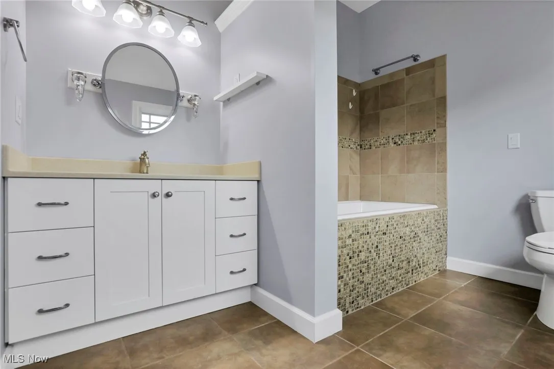 Full bathroom with tile patterned flooring, toilet, tiled shower, baseboards, and vanity