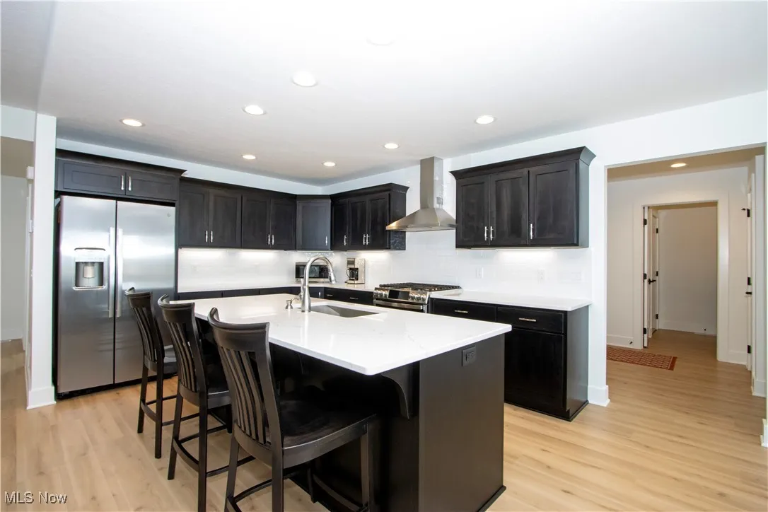 Kitchen featuring appliances with stainless steel finishes, wall chimney range hood, a sink, light wood finished floors, and recessed lighting