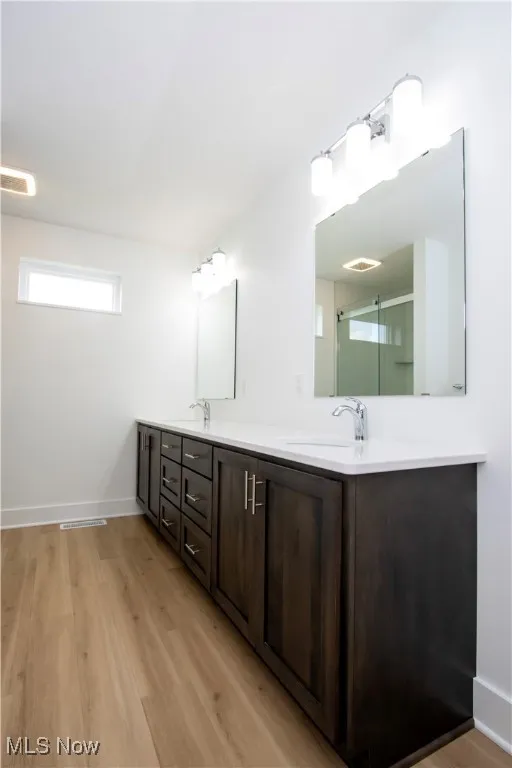 Full bath featuring double vanity, wood finished floors, a stall shower, and baseboards