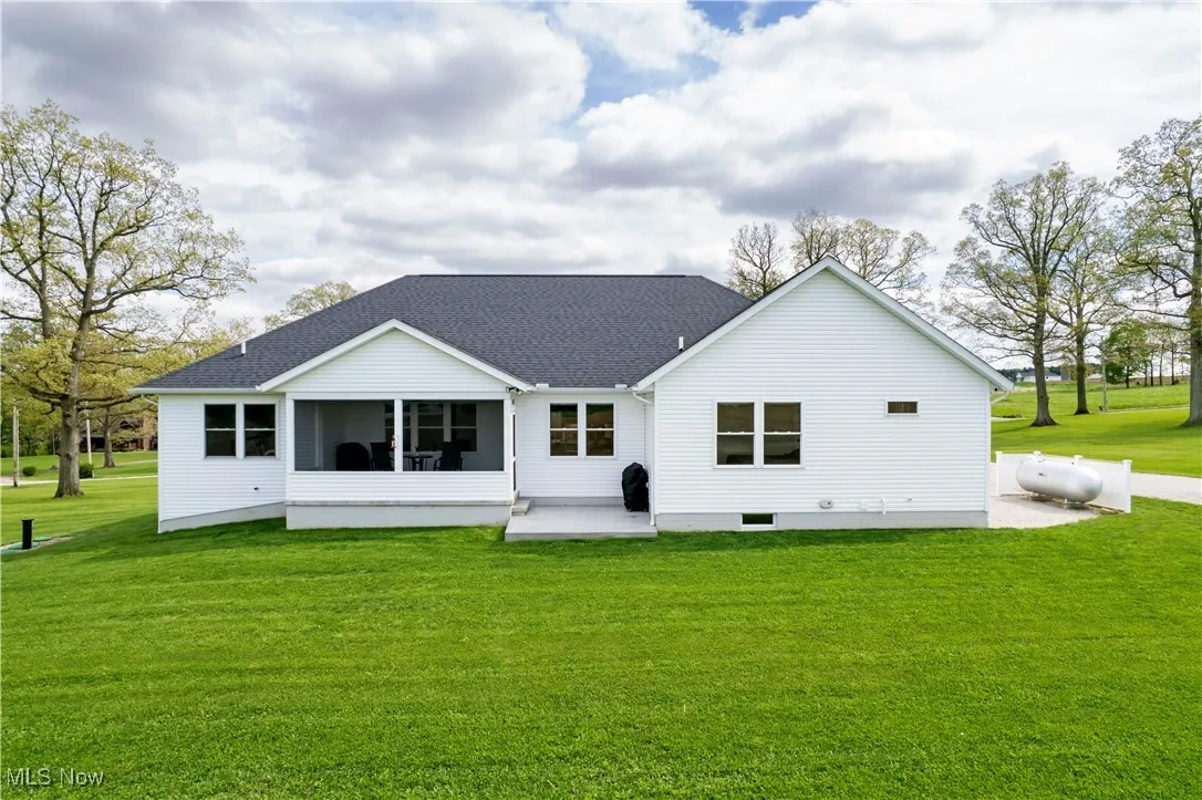 Back of property with a lawn, roof with shingles, a sunroom, and a patio