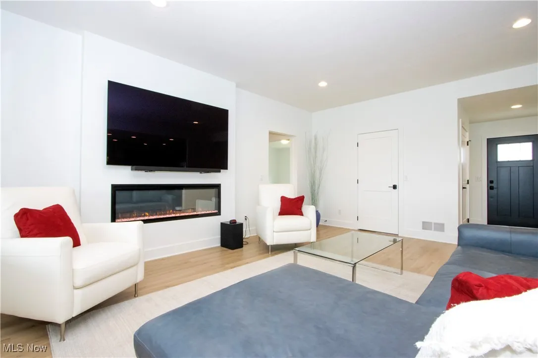 Living room with wood finished floors, recessed lighting, a glass covered fireplace, and baseboards