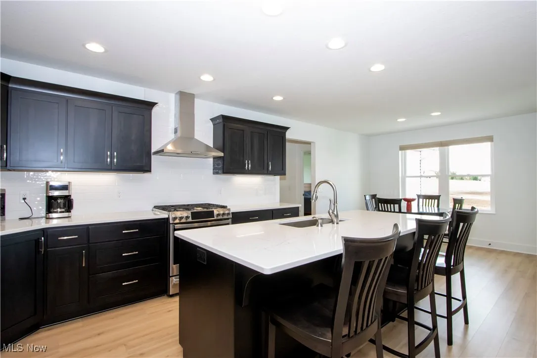 Kitchen featuring wall chimney range hood, stainless steel gas stove, a sink, a kitchen breakfast bar, and light wood finished floors