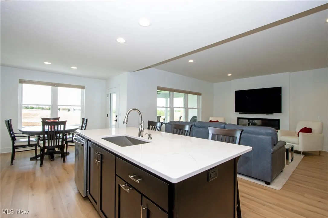 Kitchen with a sink, dark brown cabinets, light wood-style flooring, a center island with sink, and light stone counters