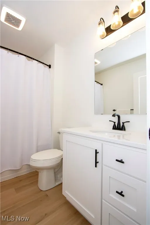 Full bathroom with wood finished floors, toilet, vanity, and a shower with curtain