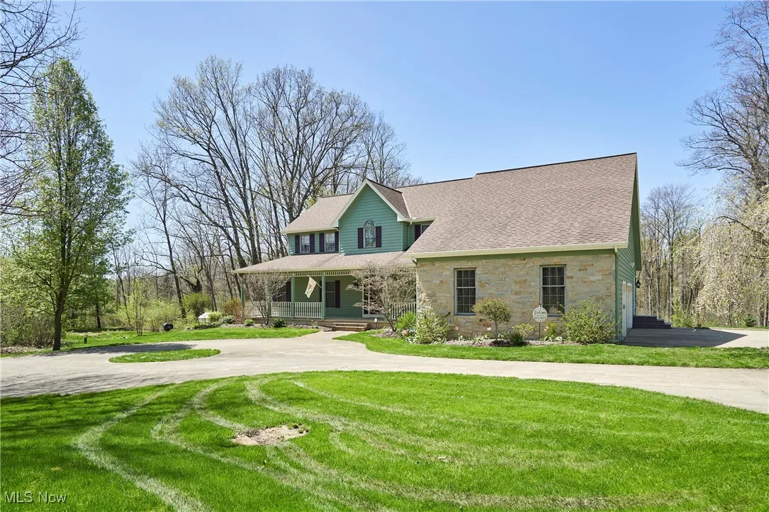View of front of property featuring stone siding, covered porch, a front yard, and roof with shingles