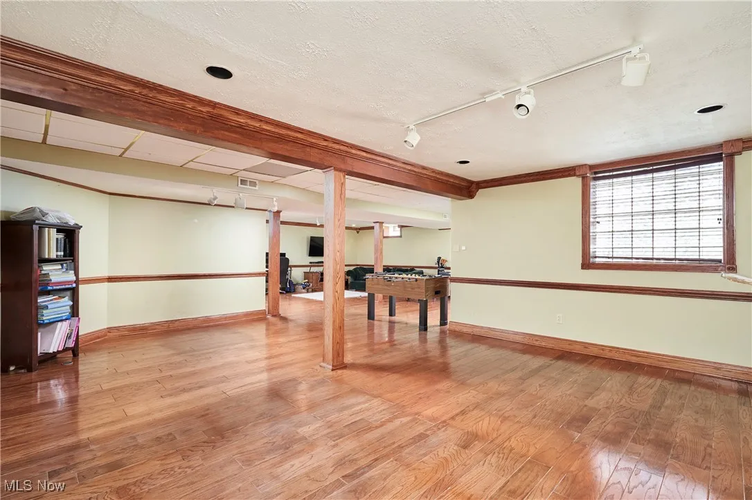 Below grade area featuring baseboards, wood finished floors, track lighting, and ornamental molding