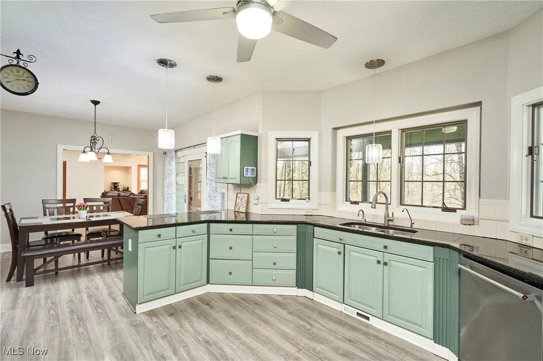 Kitchen with a sink, dishwasher, green cabinets, a peninsula, and light wood-style flooring