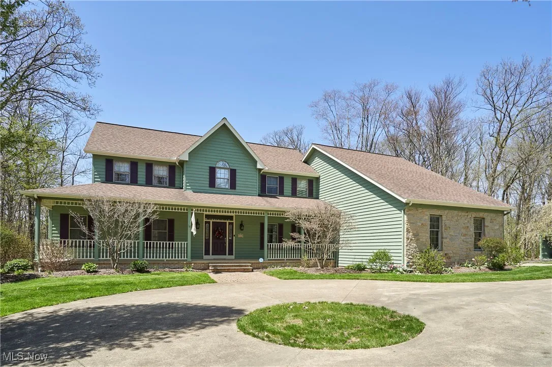 View of front of property with curved driveway, a porch, roof with shingles, and stone siding