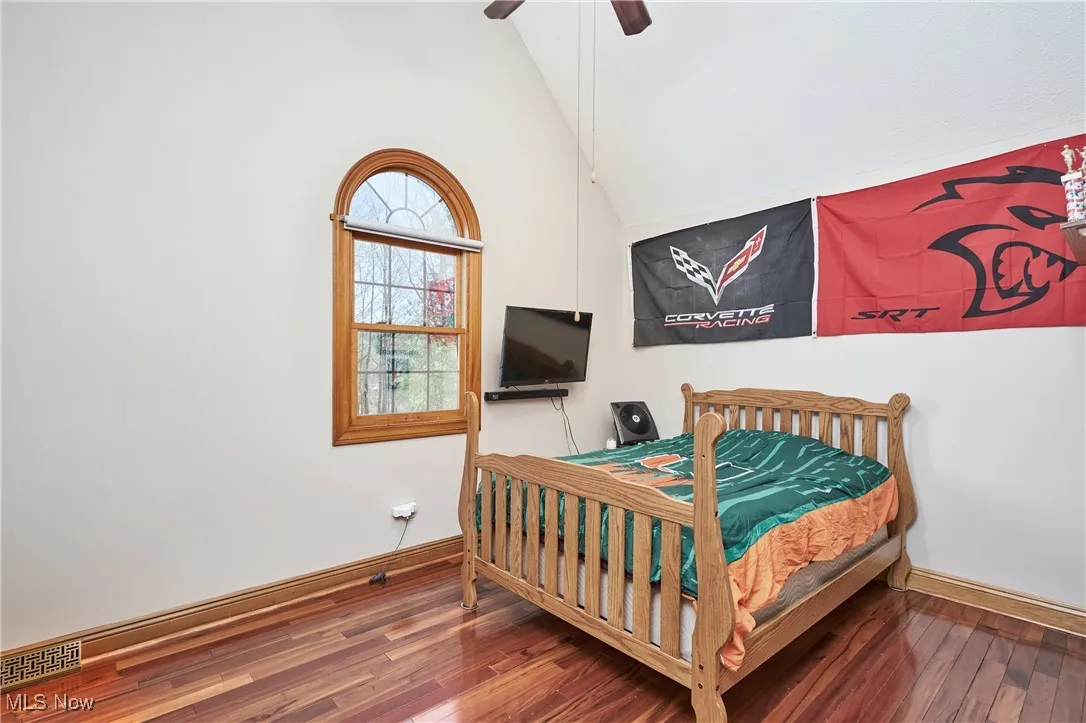 Bedroom with wood finished floors, vaulted ceiling, baseboards, and a ceiling fan