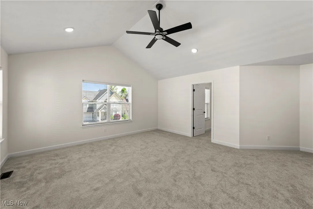 Empty room featuring light carpet, ceiling fan, baseboards, lofted ceiling, and recessed lighting