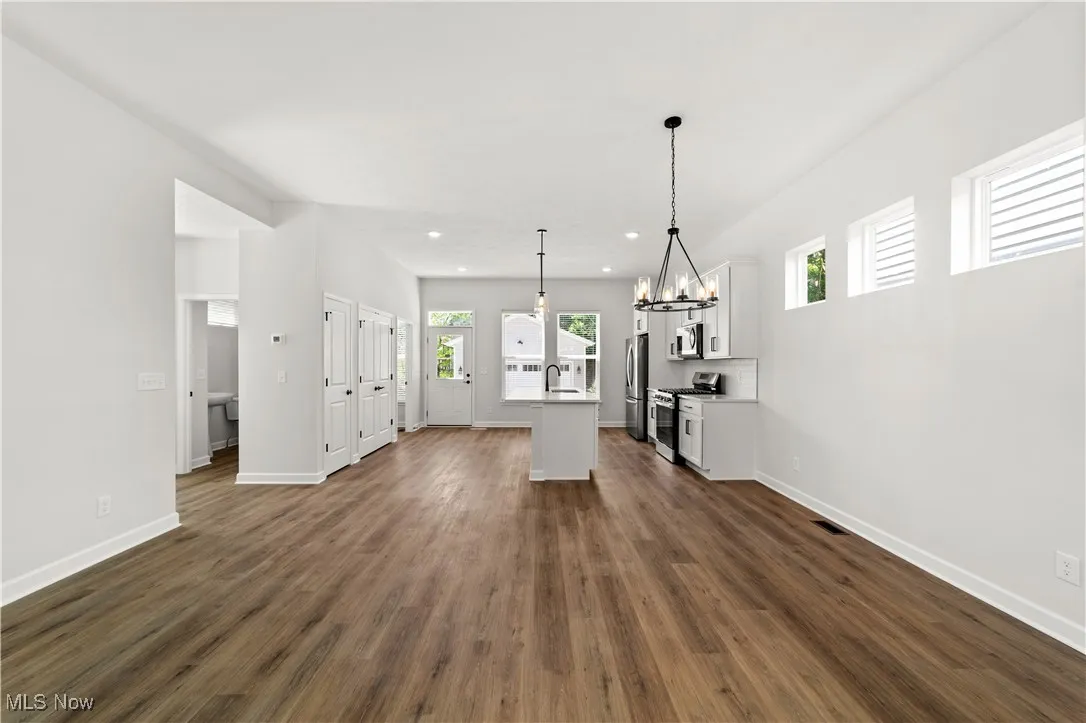 Unfurnished living room with a chandelier, plenty of natural light, recessed lighting, dark wood-style flooring, and baseboards