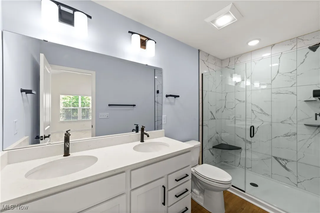 Bathroom featuring a marble finish shower, wood finished floors, toilet, and double vanity