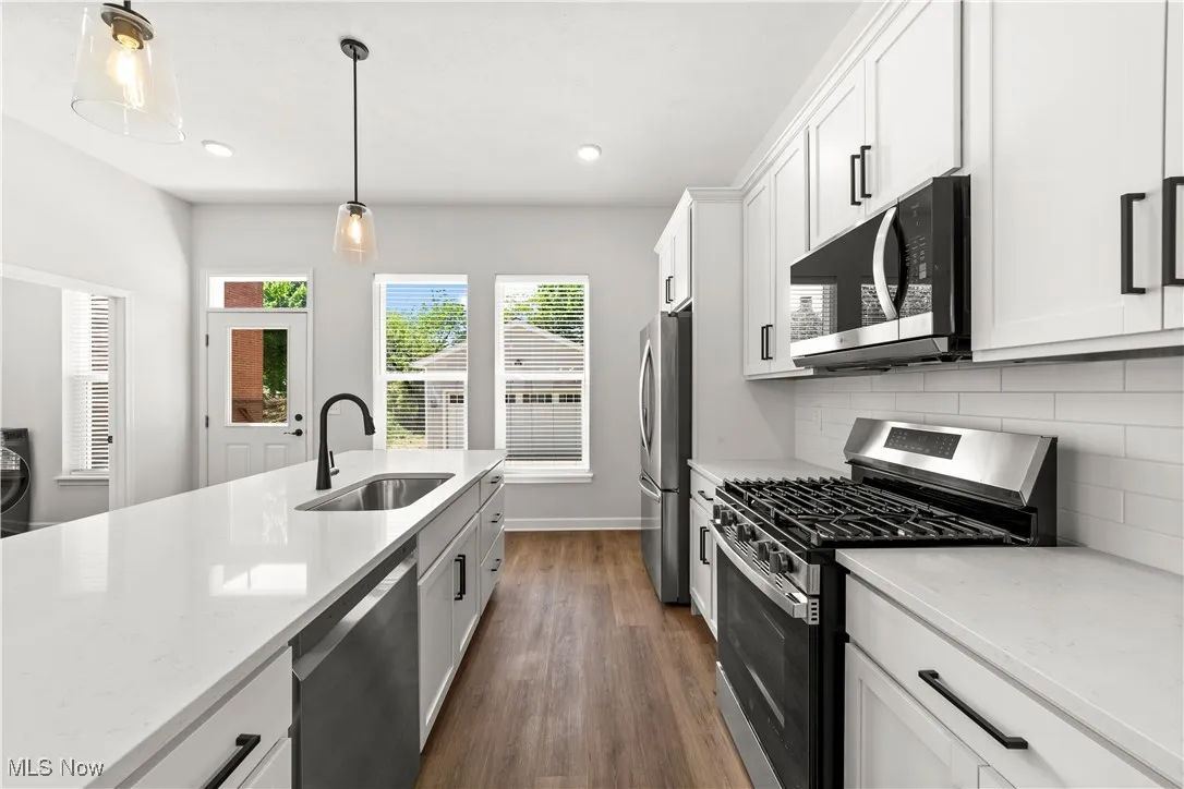 Kitchen featuring stainless steel appliances, a sink, dark wood-style floors, backsplash, and decorative light fixtures