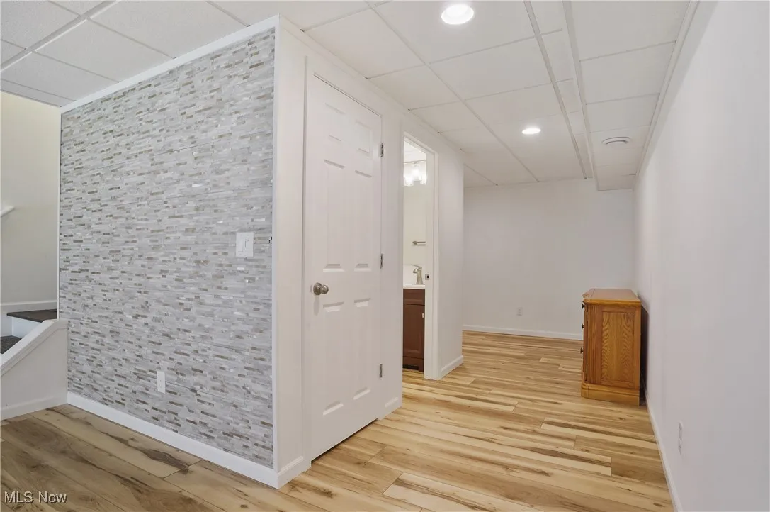 Hall featuring light wood-style flooring, baseboards, and a paneled ceiling