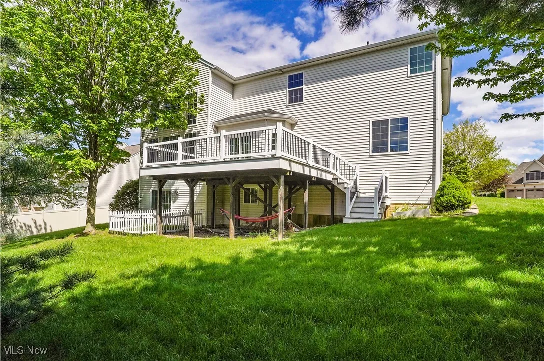 Rear view of house featuring stairway, a wooden deck, fence, and a lawn