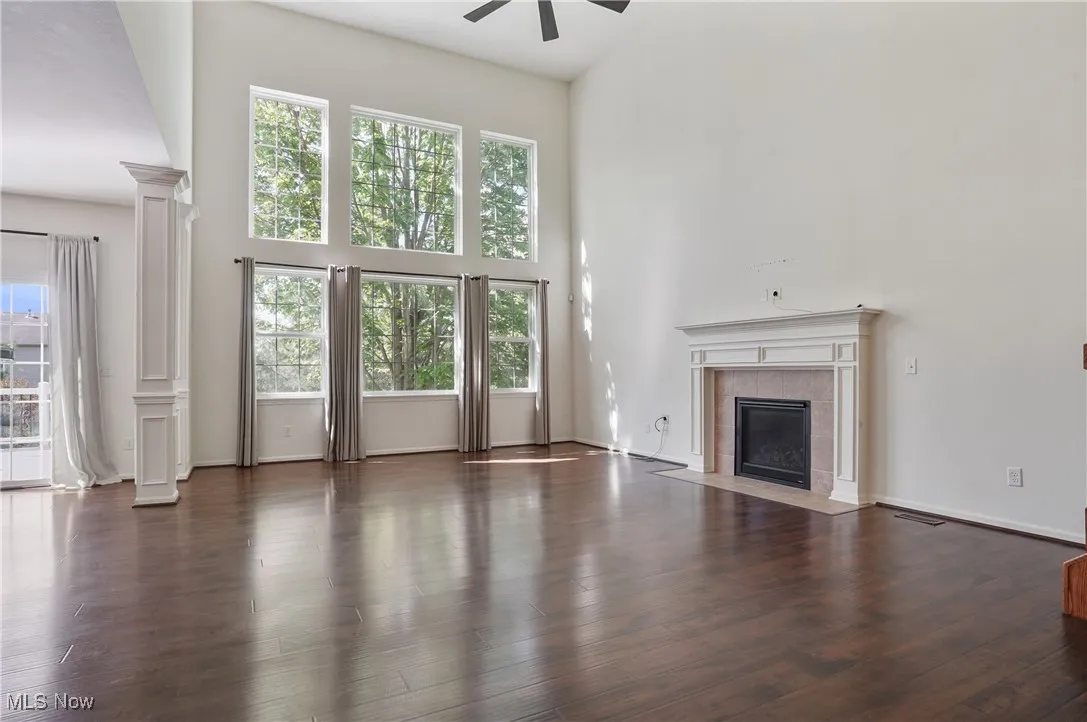 Unfurnished living room featuring decorative columns, a ceiling fan, a fireplace, and a towering ceiling