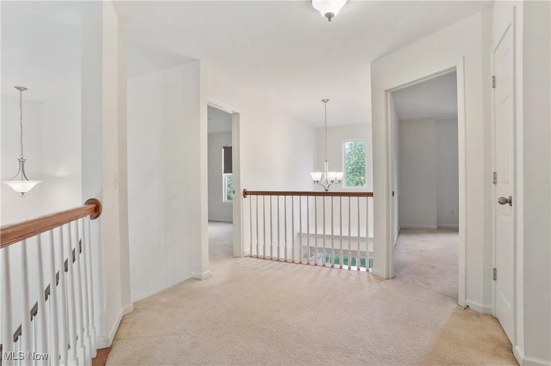 Hall featuring baseboards, an upstairs landing, a chandelier, and light colored carpet