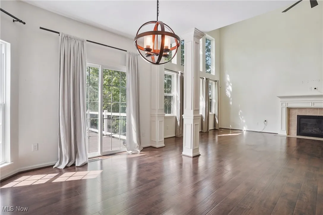 Unfurnished living room featuring a tile fireplace, a notable chandelier, ornate columns, and wood finished floors