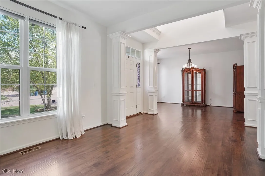 Empty room with a notable chandelier, baseboards, dark wood-style flooring, visible vents, and decorative columns