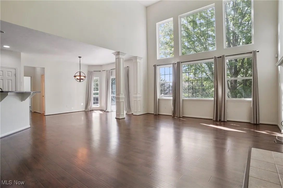 Unfurnished living room featuring baseboards, dark wood finished floors, an inviting chandelier, decorative columns, and a towering ceiling