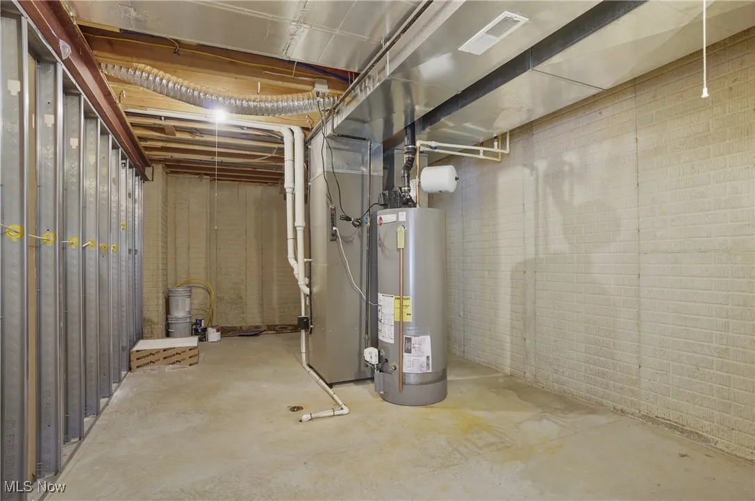 Unfinished basement with brick wall, gas water heater, and visible vents