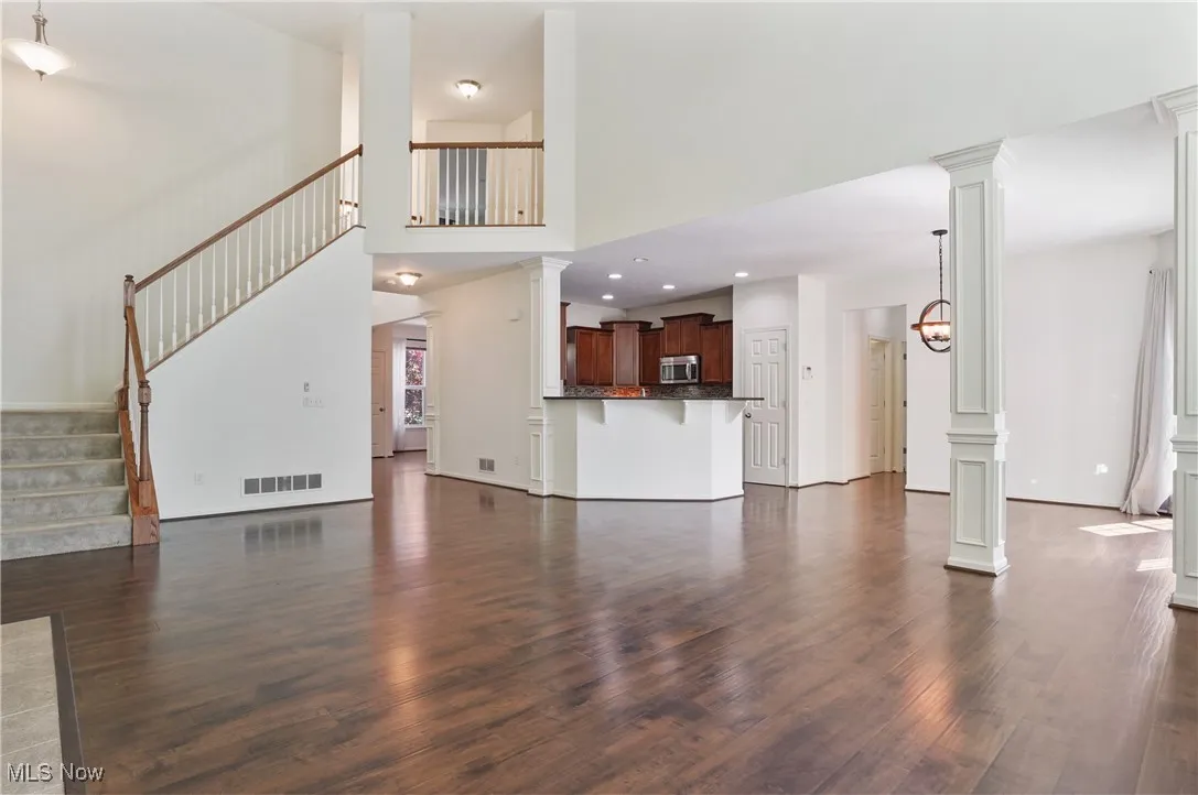 Unfurnished living room with recessed lighting, dark wood finished floors, visible vents, decorative columns, and stairway