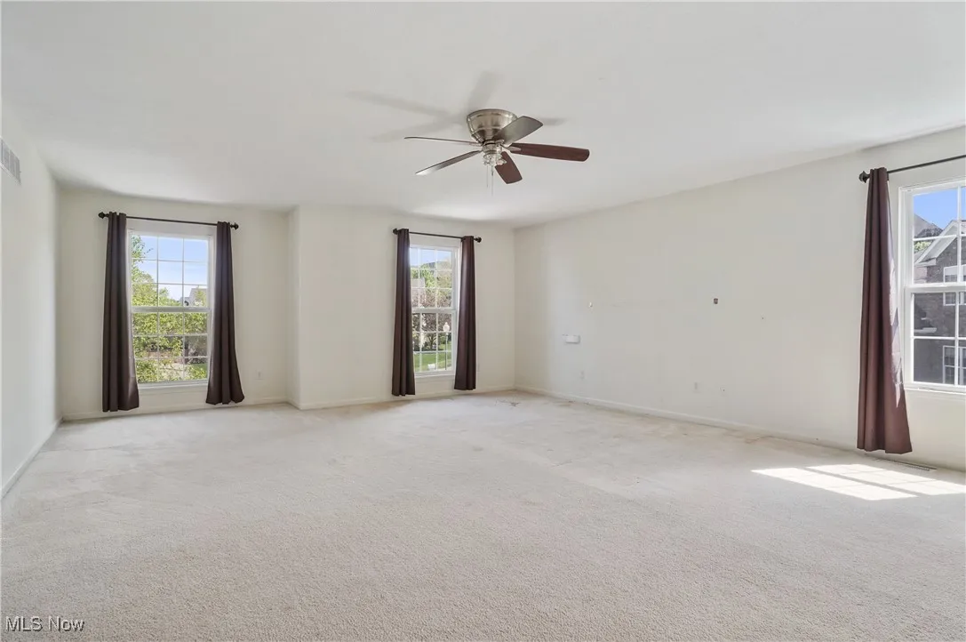 Unfurnished room featuring visible vents, a ceiling fan, a healthy amount of sunlight, and light carpet