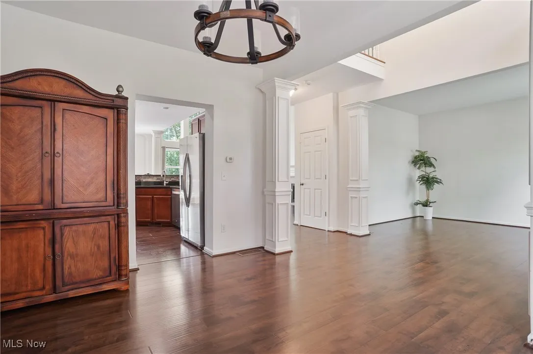 Unfurnished room featuring an inviting chandelier, decorative columns, and dark wood-style floors