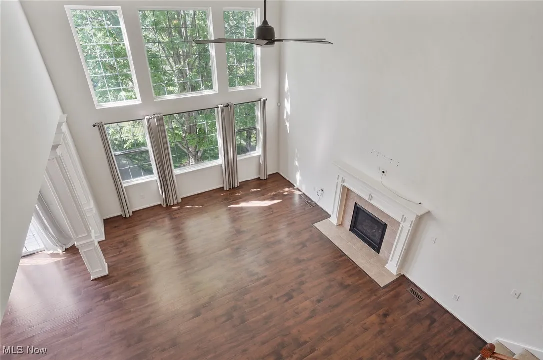 Unfurnished living room featuring wood finished floors, a high ceiling, visible vents, ceiling fan, and a high end fireplace