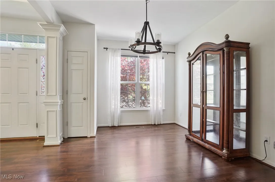 Unfurnished dining area featuring a chandelier, dark wood-style flooring, baseboards, and ornate columns