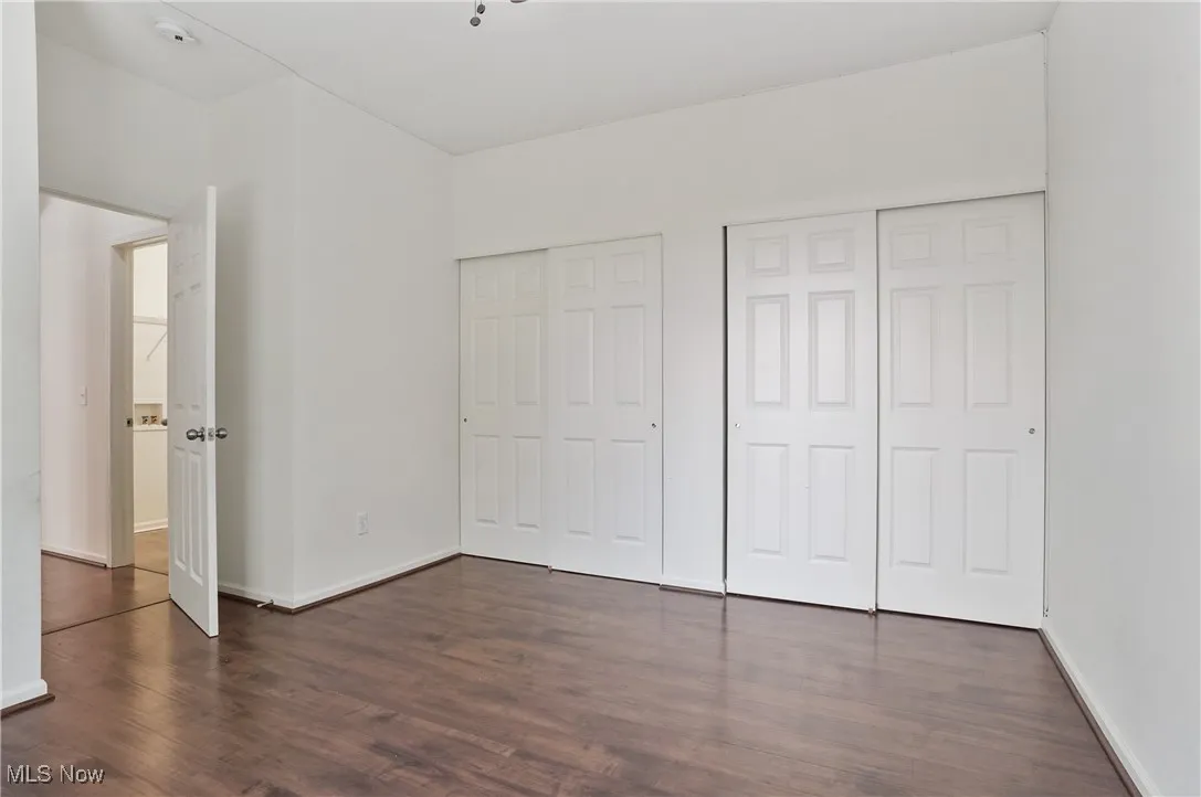 Unfurnished bedroom featuring dark wood-style flooring, baseboards, and multiple closets