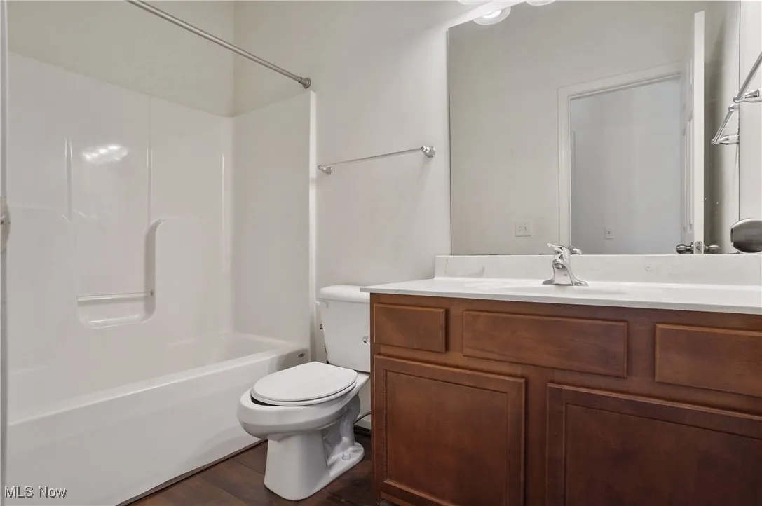 Bathroom with toilet, vanity, tub / shower combination, and wood finished floors