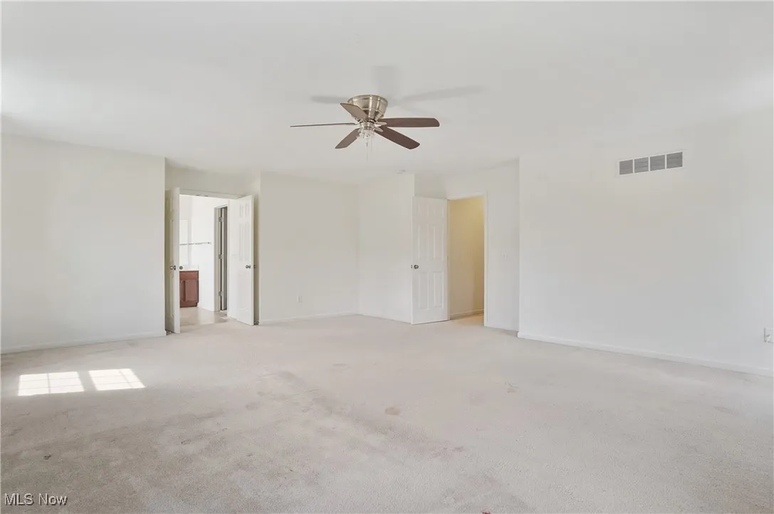 Empty room featuring light carpet, baseboards, a ceiling fan, and visible vents