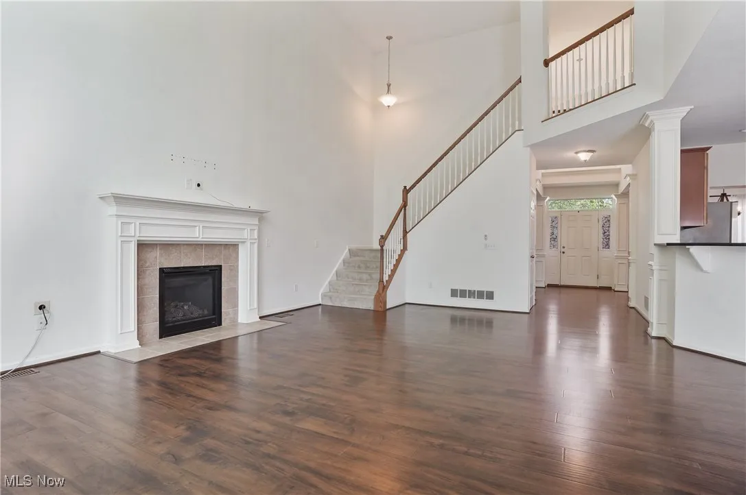 Unfurnished living room featuring a tile fireplace, visible vents, wood finished floors, and stairway
