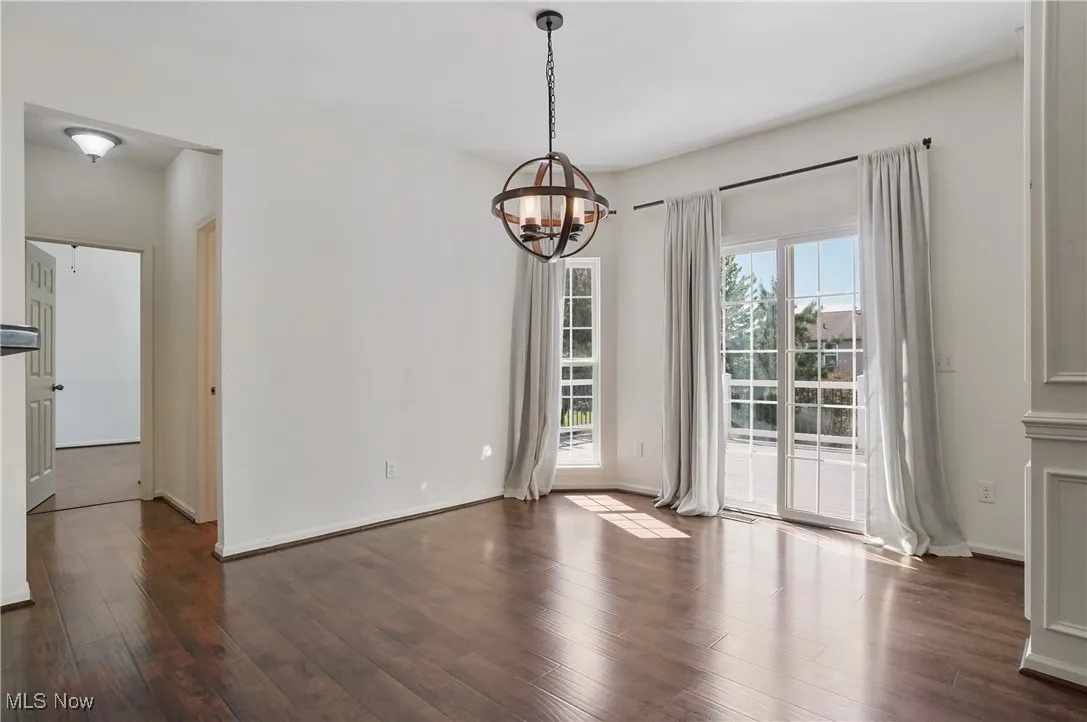 Unfurnished dining area featuring baseboards, a notable chandelier, and dark wood-style floors