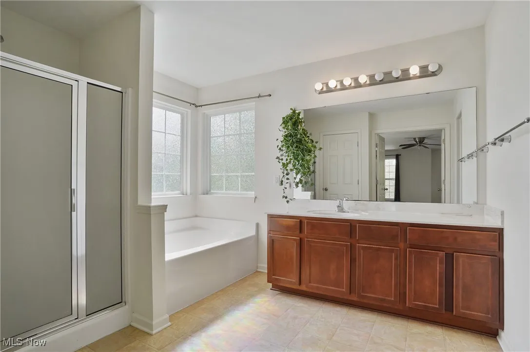Full bathroom featuring a ceiling fan, a bath, baseboards, a shower stall, and vanity