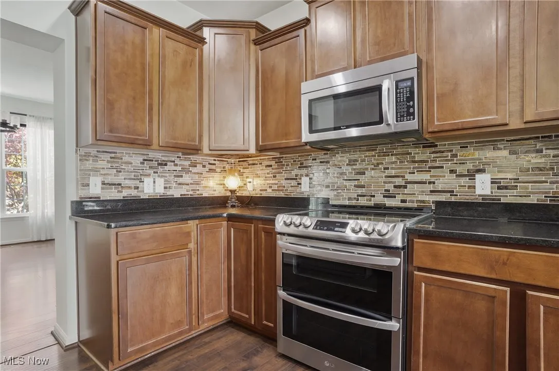 Kitchen with decorative backsplash, brown cabinets, stainless steel appliances, dark stone counters, and dark wood-style floors