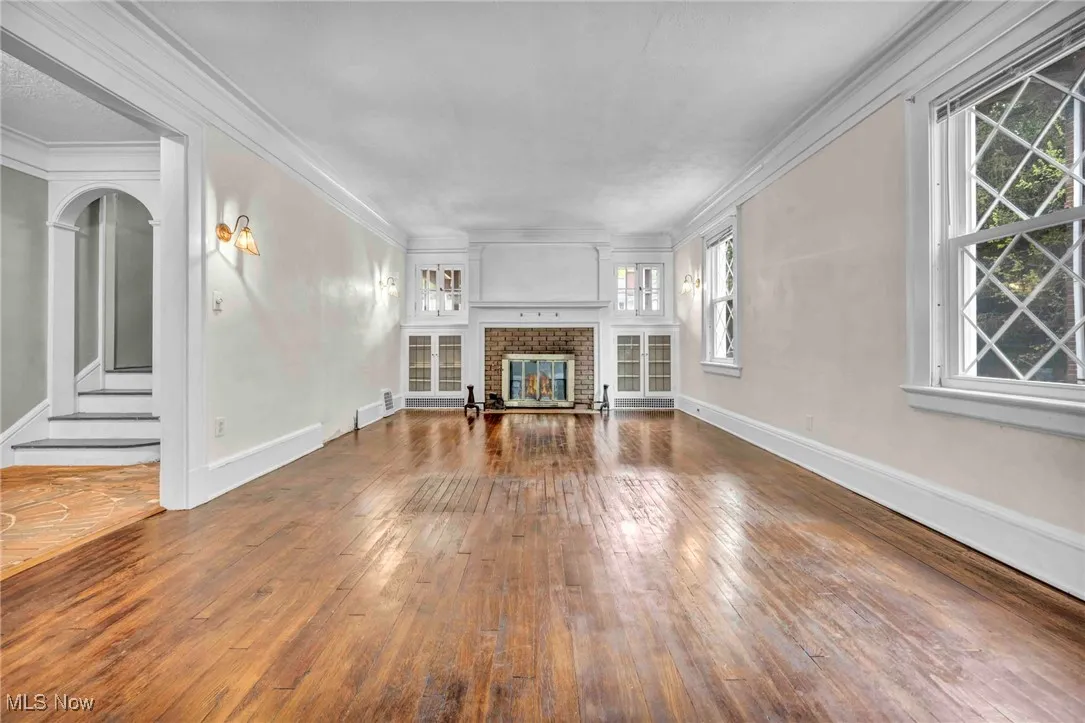 Unfurnished living room with healthy amount of natural light, hardwood / wood-style flooring, a brick fireplace, and crown molding