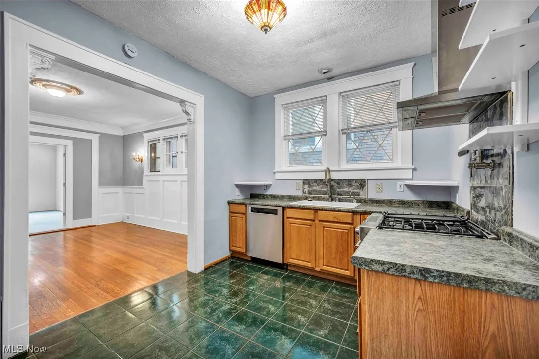 Kitchen with dishwasher, a sink, wall chimney exhaust hood, brown cabinetry, and a textured ceiling
