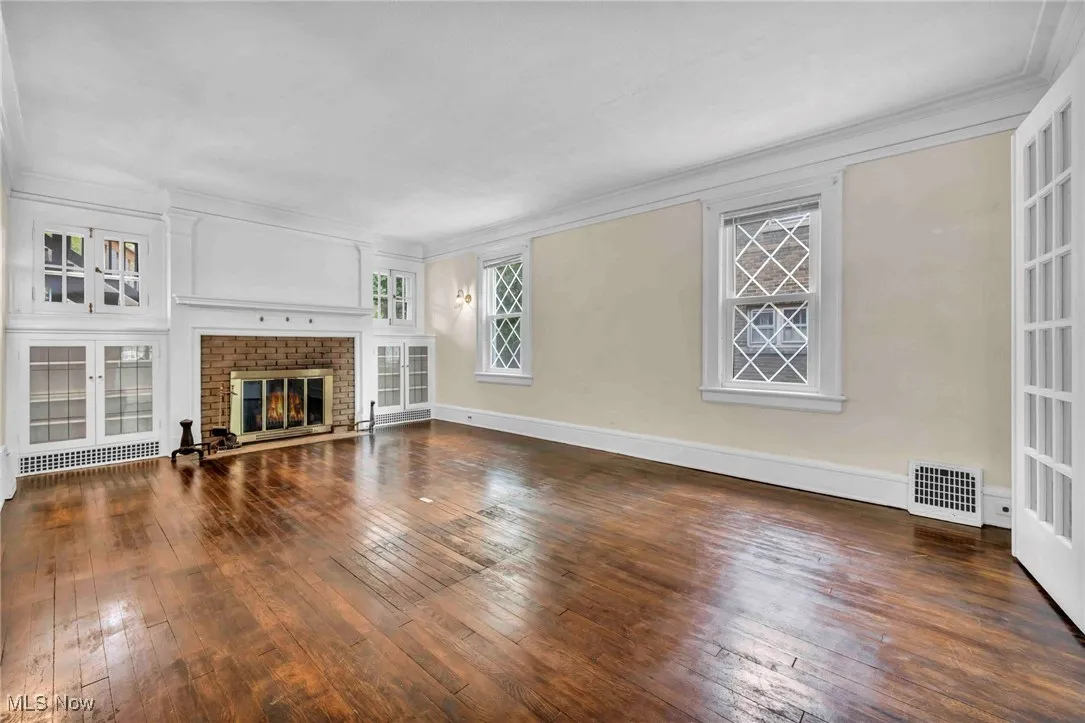 Unfurnished living room with hardwood / wood-style flooring, crown molding, a fireplace, and baseboards