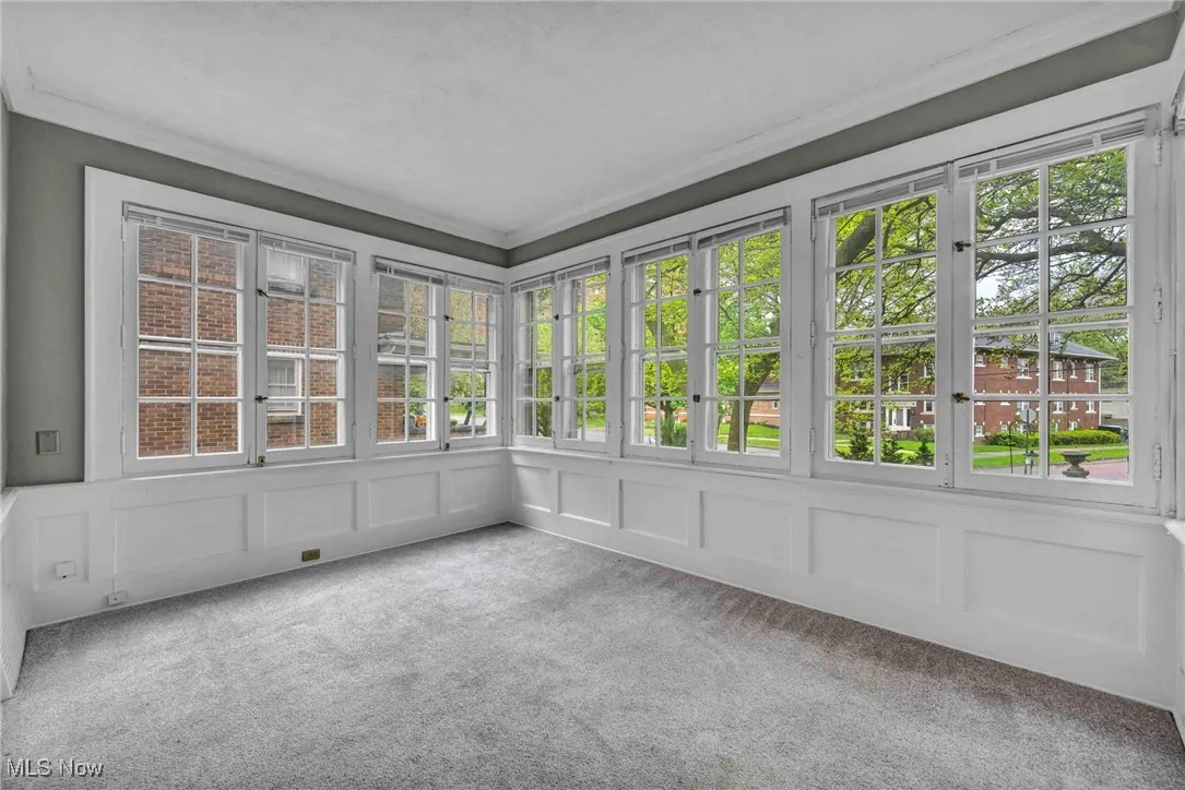 Unfurnished sunroom with a decorative wall, carpet flooring, ornamental molding, and french doors