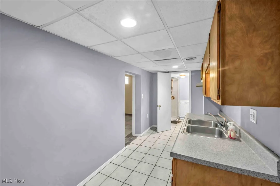Kitchen featuring a sink, a drop ceiling, brown cabinetry, light tile patterned flooring, and light countertops