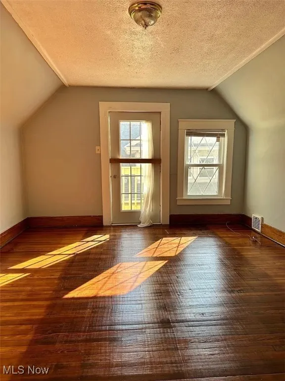 Bedroom featuring hardwood / wood-style flooring, lofted ceiling, healthy amount of natural light, a textured ceiling, and baseboards