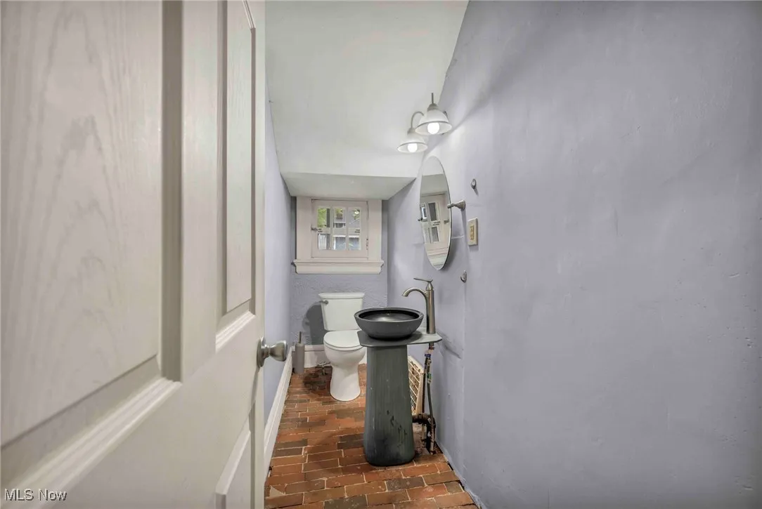 Half bathroom with brick floors, toilet, and a sink